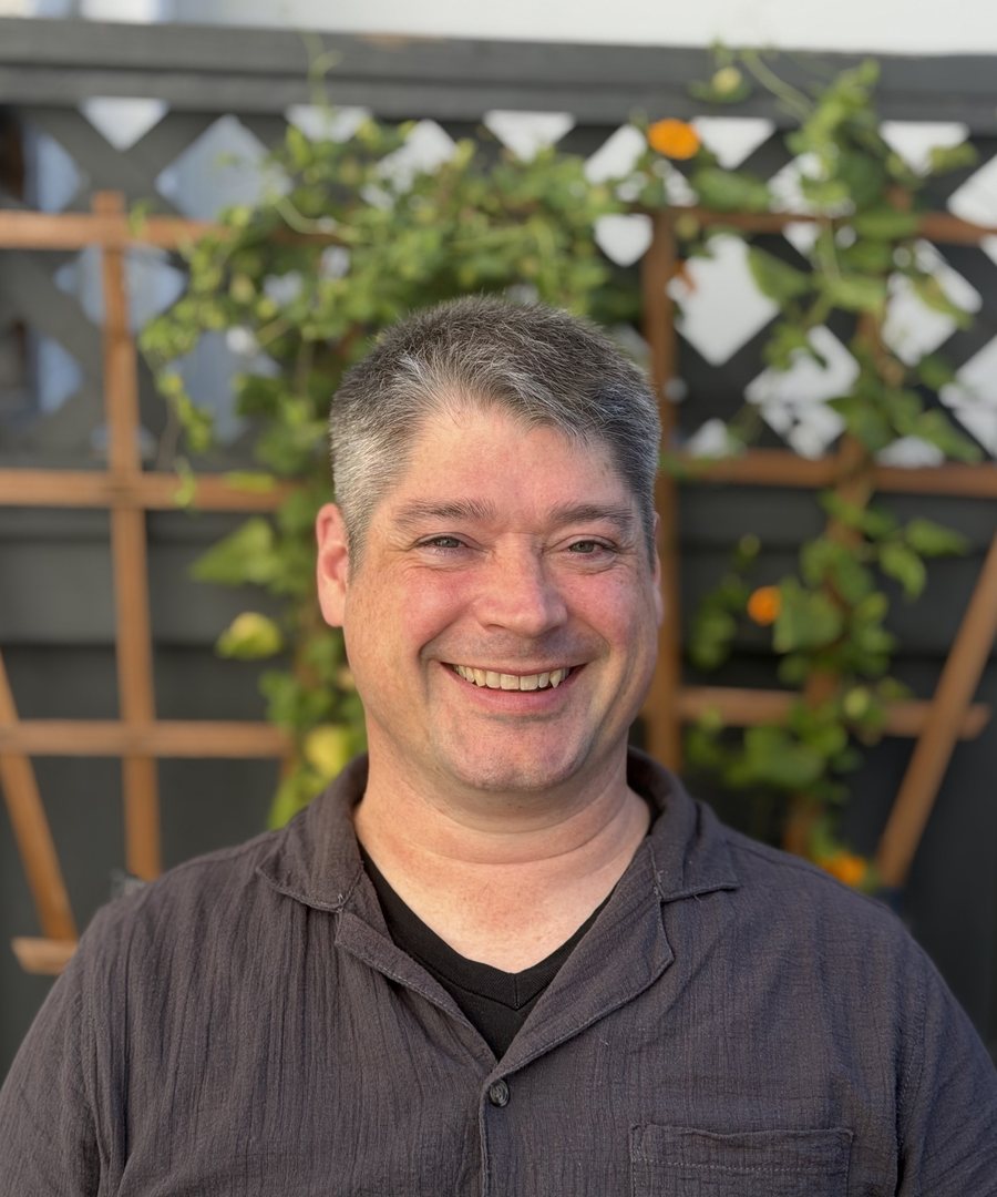 Jamie Bonner, smiling, in front of a garden trellis with climbing vines